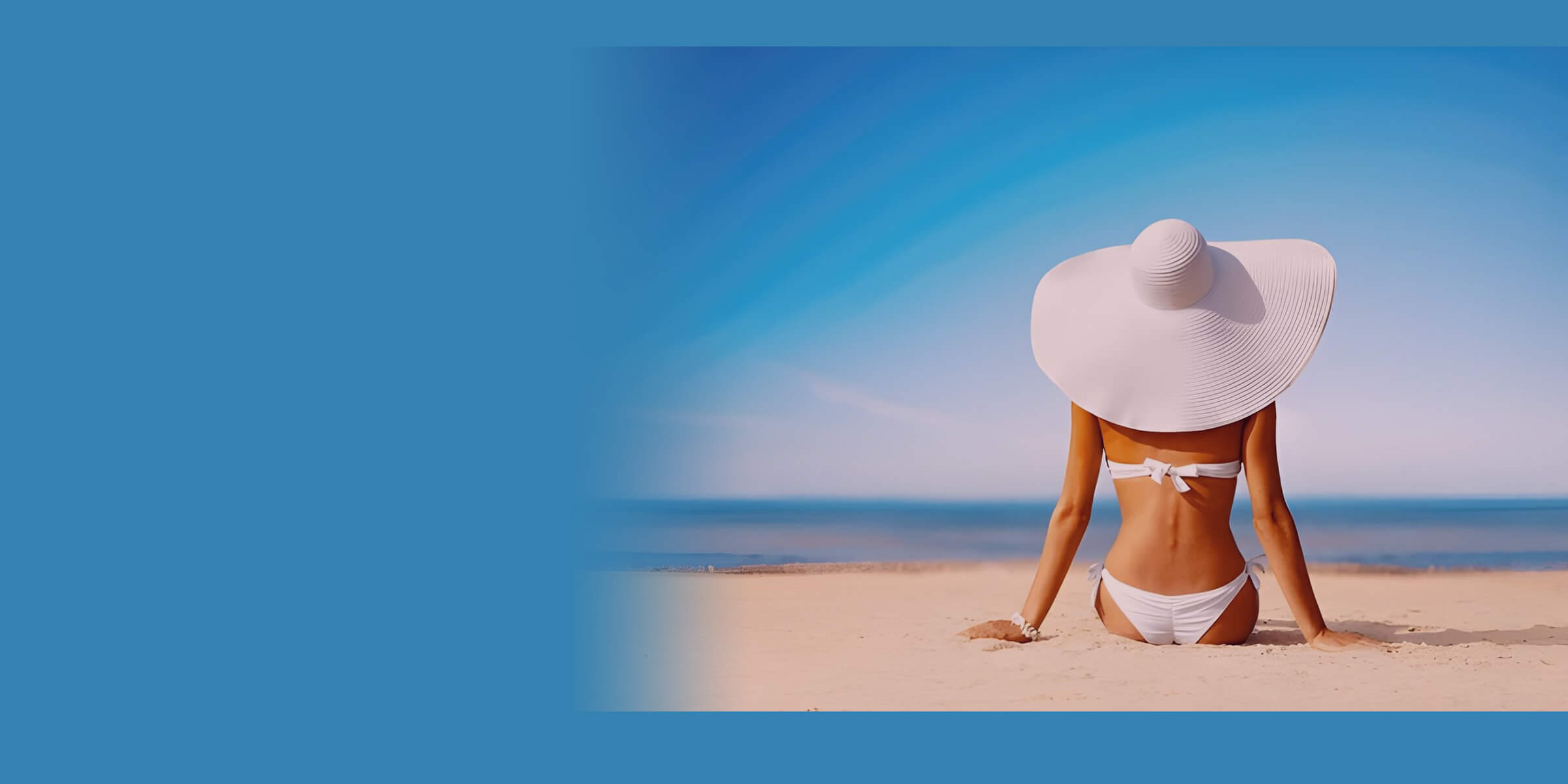 A woman in a white bikini and wide-brimmed sun hat sitting on sunlit sand, facing a blue sea and sky.