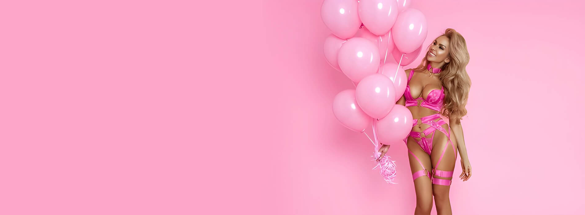 A smiling model in a pink strappy lingerie set holds a cluster of pink balloons against a soft pink backdrop.