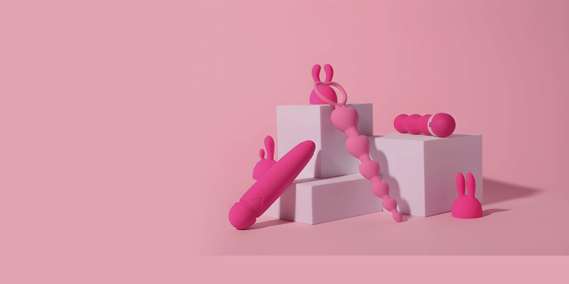 Pink silicone sex toys — a rabbit-eared vibrator, anal beads, a wand and a bullet — arranged on pale-pink pedestals against a pink backdrop.
